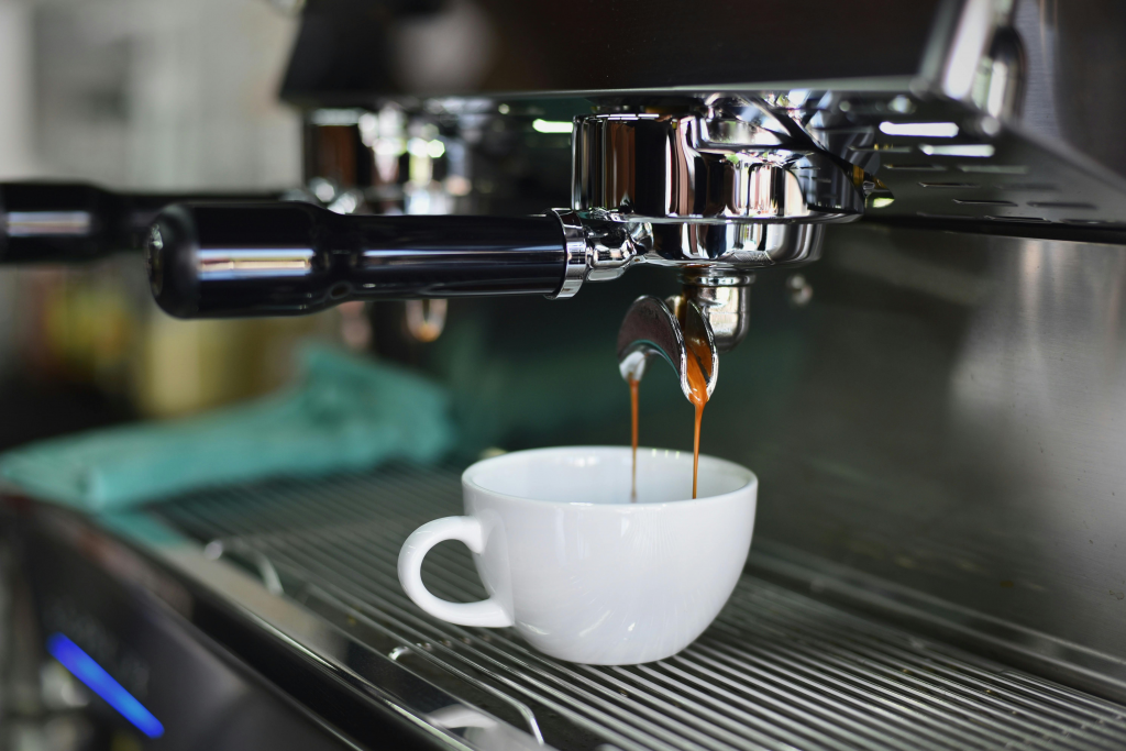 an espresso machine dropping a double espresso into a white demi-tasse