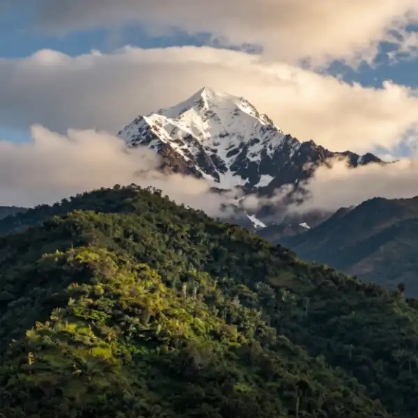 Mount Kenya — snow-capped peak rising above lush green slopes with dramatic clouds.