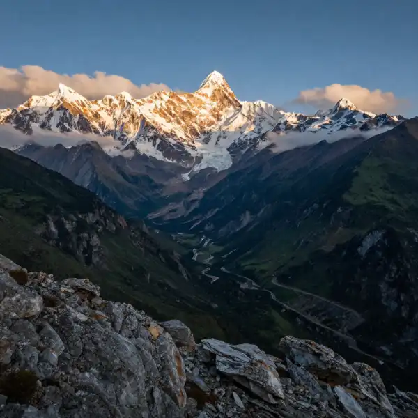 A dramatic landscape of the Andes mountains featuring snow-capped peaks rising above deep green valleys, with rugged rocky terrain in the foreground, wispy clouds threading between the summits, and golden morning light illuminating the glaciers — conveying the vast scale and altitude of the range.