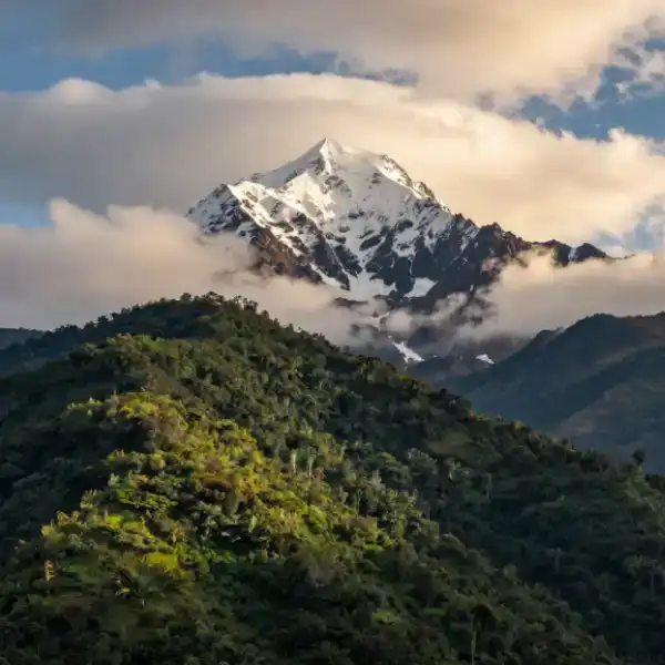 Mount Kenya — snow-capped peak rising above lush green slopes with dramatic clouds.