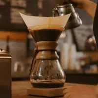 The Chemex coffee brewing method showing the glass bottle with the thick filter paper and boiling water being poured into the ground coffee